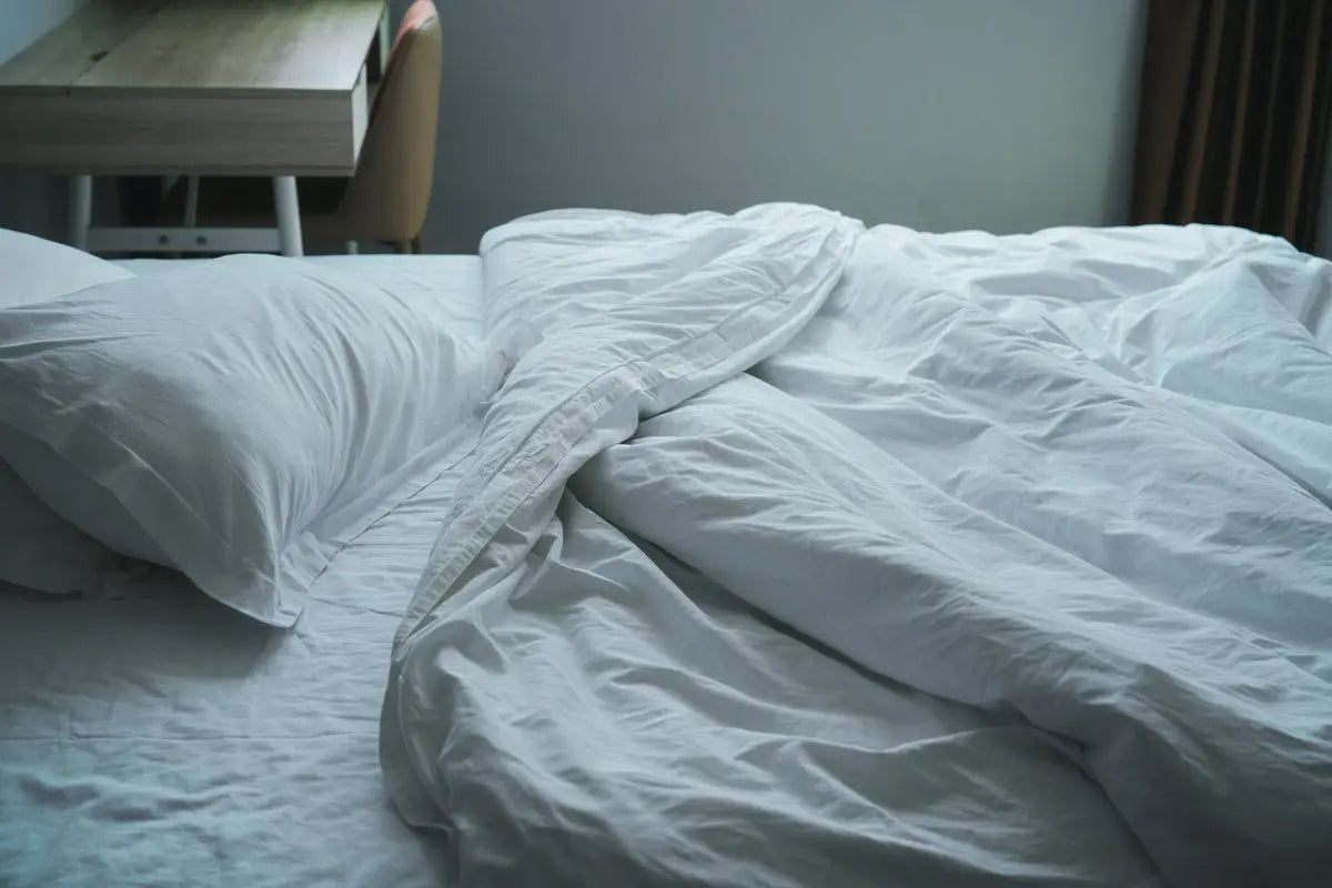 An unmade bed with white sheets and a night stand