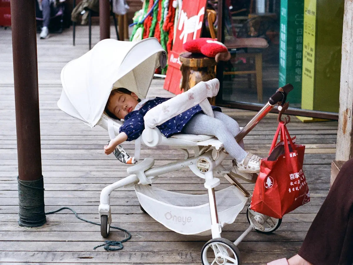 A young child sleeps soundly in a stroller outdoors.