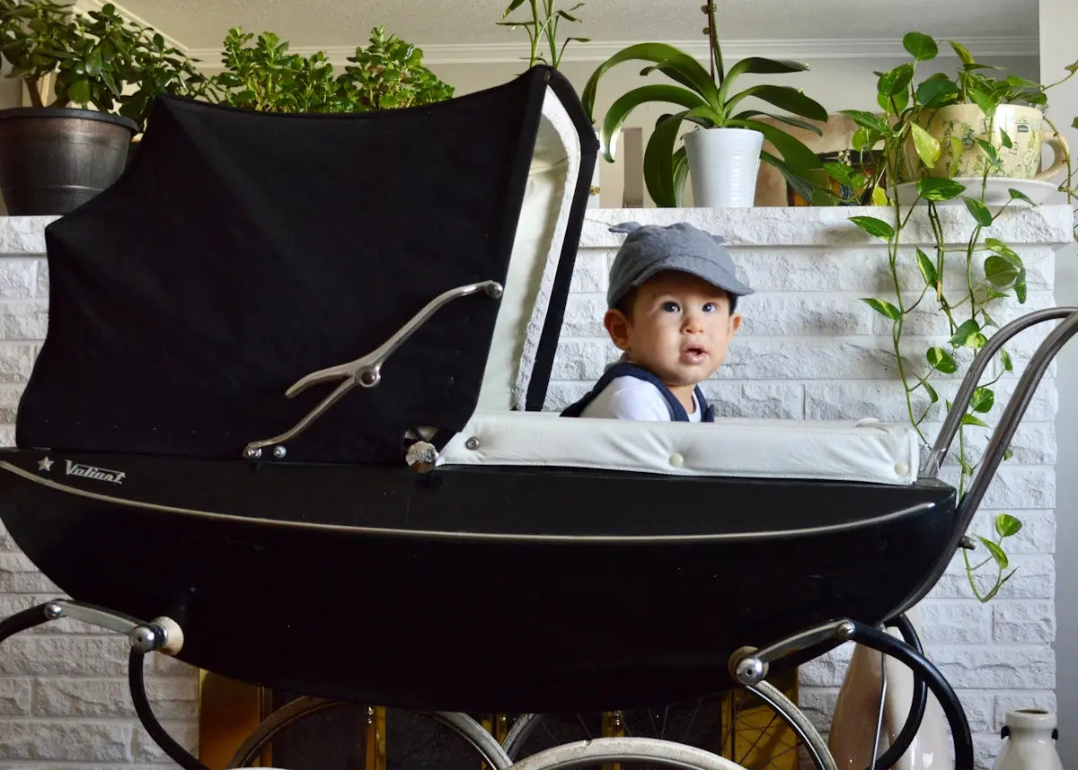 baby in white hat lying on black stroller